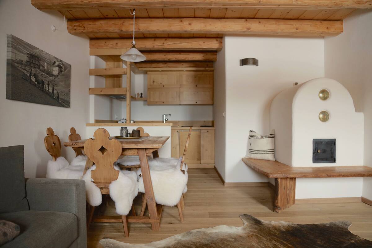 A cozy interior with a wooden dining table, white furry chairs, a grey sofa, and a large fur rug.
