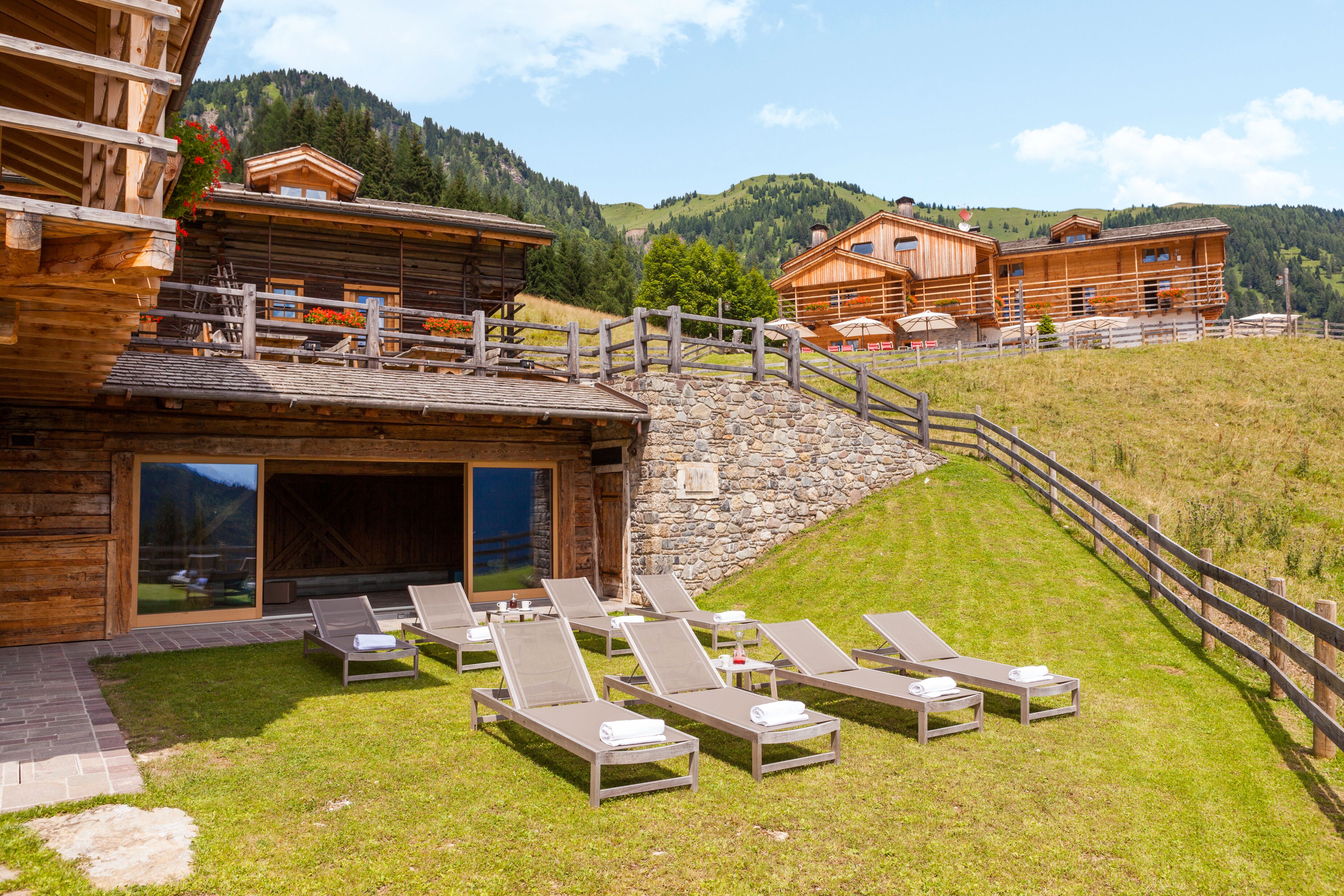 Un chalet en bois avec un mur en pierre et une terrasse en bois équipée de chaises longues.
