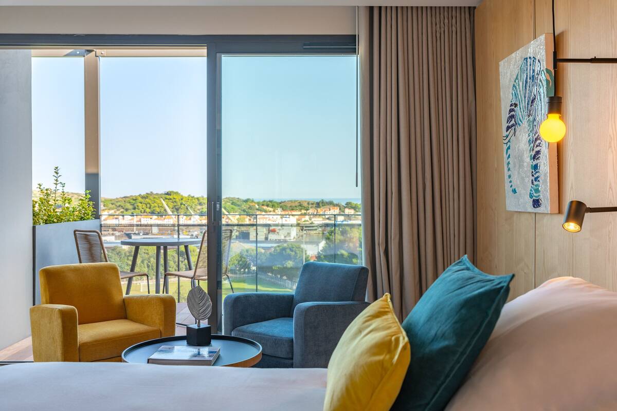 Een hotelkamer met een groot raam, een bed, een bijzettafeltje en twee stoelen.