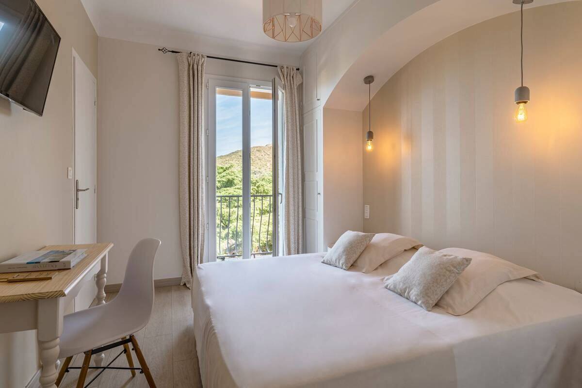 Een slaapkamer met een groot bed, een bureau en een stoel, met uitzicht op een balkon en glooiende heuvels.