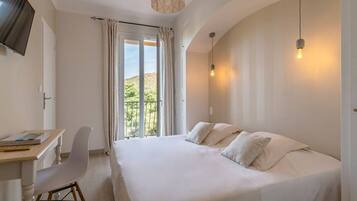 Een slaapkamer met een groot bed, een bureau en een stoel, met uitzicht op een balkon en glooiende heuvels.
