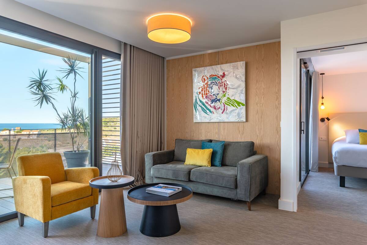 Een moderne hotelkamer met een bank, fauteuil en uitzicht op de oceaan.