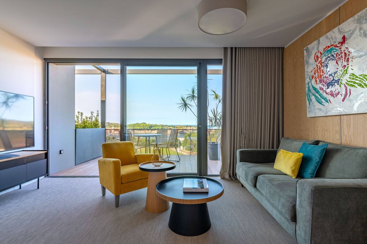 Een moderne woonkamer met een bank, fauteuil, salontafel en een groot raam met uitzicht op de omgeving.