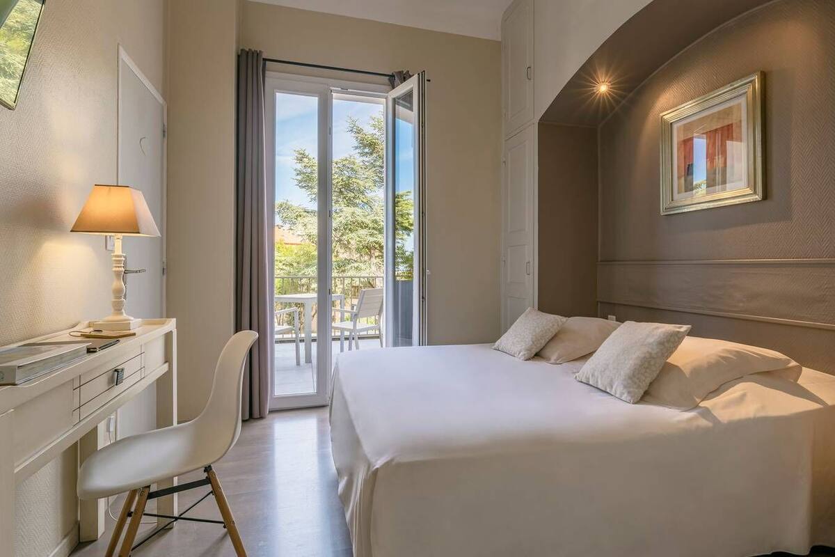 Een hotelkamer met een bed, een bureau met lamp, een stoel en een balkon met tafel en stoelen.