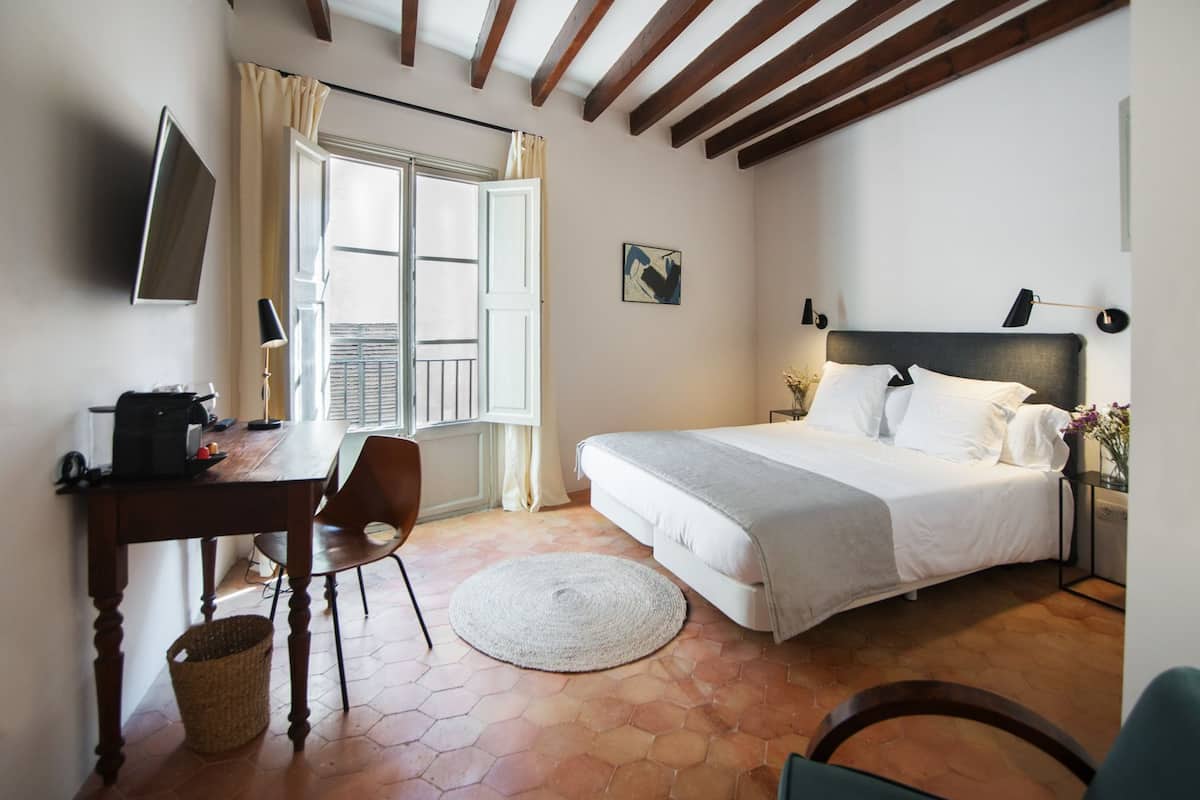 A bedroom with a bed, a desk, a chair, a TV, and a window with curtains.