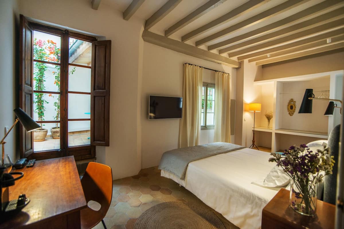 A bedroom with a bed, a desk, a chair, a TV, a lamp, and a window with curtains.