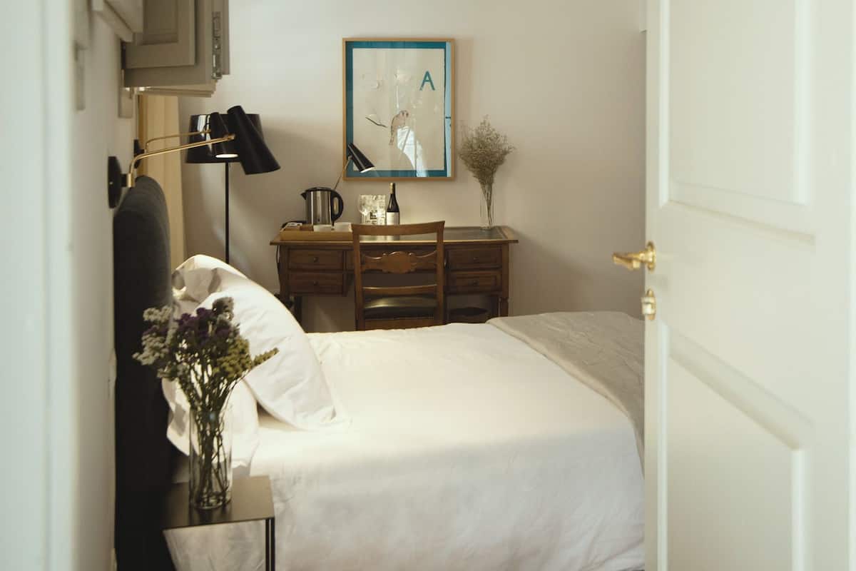 A bedroom with a bed, a desk, a chair, a lamp, and a framed picture on the wall.