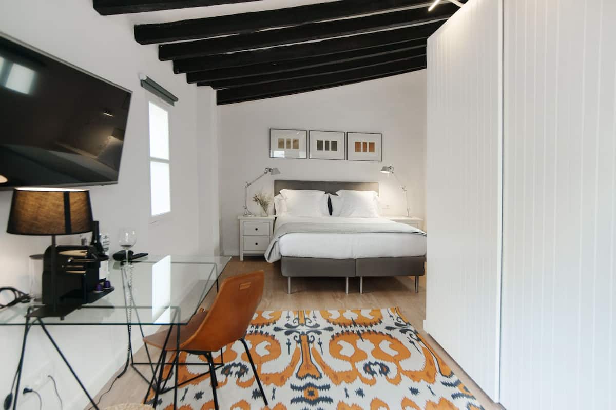 A modern bedroom with a bed, bedside tables, a desk with a chair, a TV, and a patterned rug.