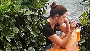 A person sitting at a wooden table with a drink, overlooking a rocky coastline. - Lanta Hostel - Adults Only (Ko Lanta)