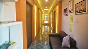 A hotel lobby with a long corridor, a reception desk, a waiting area with a sofa, and framed pictures on the wall. - Lanta Hostel - Adults Only (Ko Lanta)
