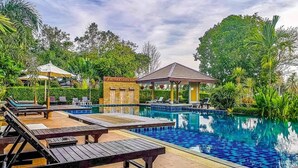A swimming pool with lounge chairs and a gazebo, surrounded by lush greenery. - Lanta Hostel - Adults Only (Ko Lanta)