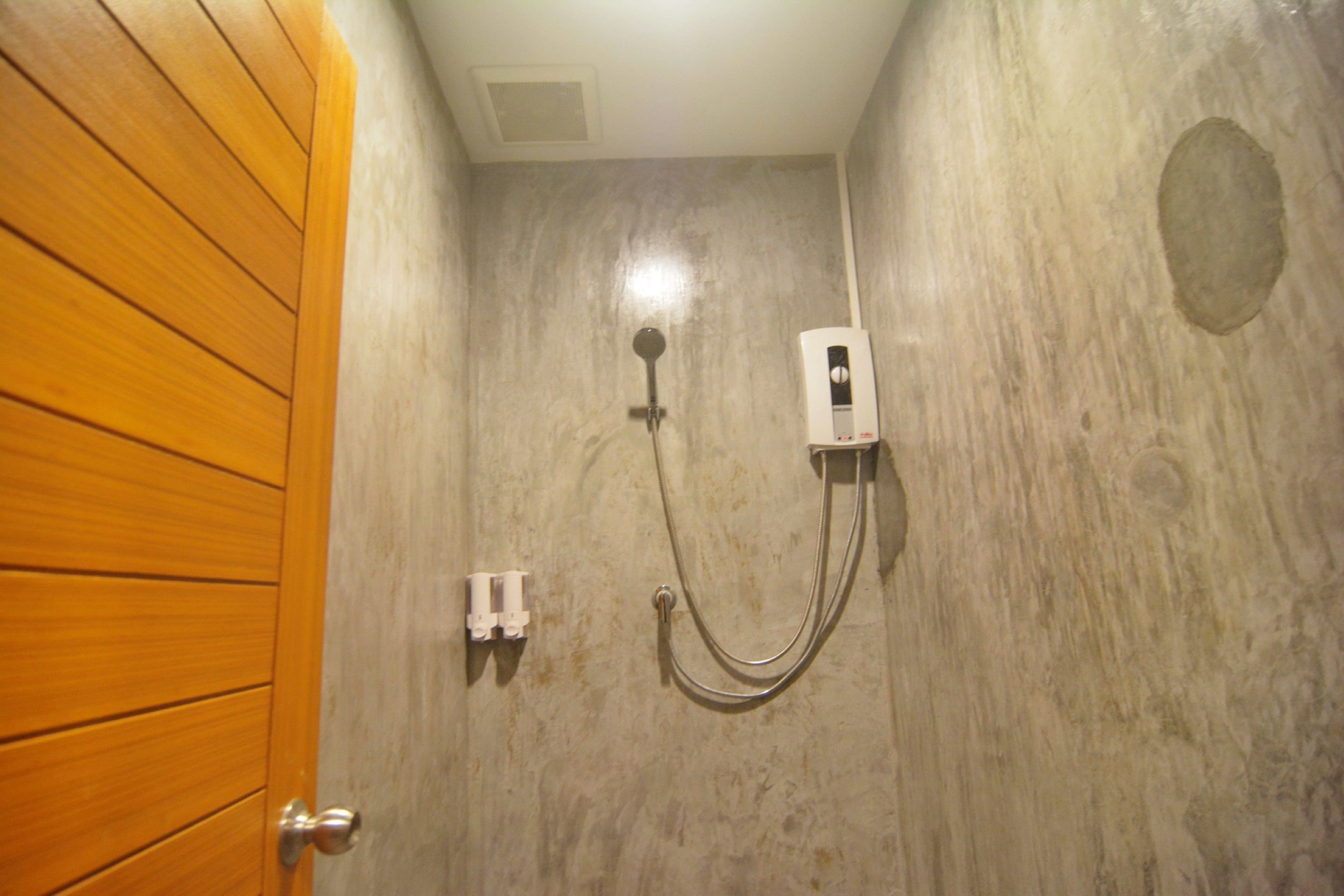 Un baño con puerta de madera, ducha con cabezal de ducha manual y panel de control en la pared.