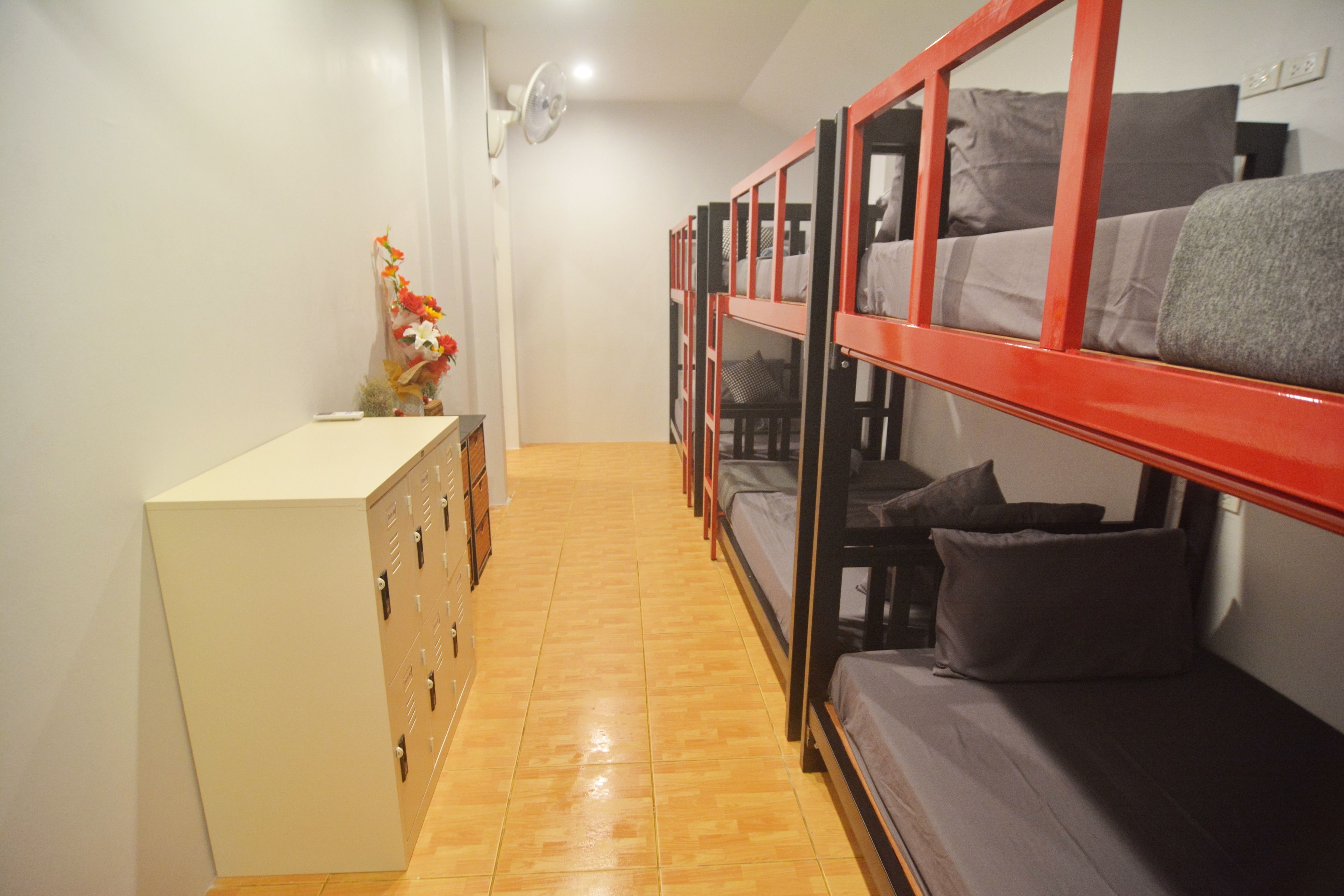 A dormitory room with bunk beds, a dresser, and a wall-mounted fan.