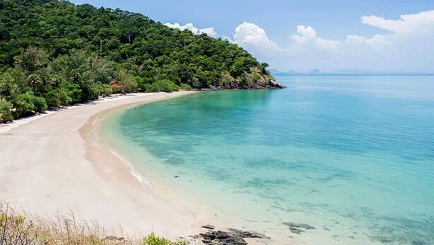 A beach with clear turquoise water, a sandy shore, and a forested hillside. - Lanta Hostel - Adults Only (Ko Lanta)