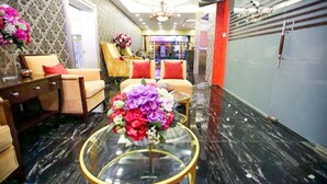 Un vestíbulo de hotel con una zona de estar, una mesa de centro de vidrio con flores y un televisor montado en la pared.