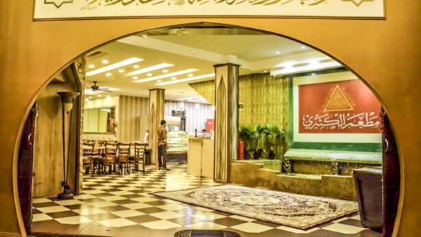 Un vestíbulo de hotel con piso de cuadros, una recepción y una amplia pared decorativa con escritura árabe.