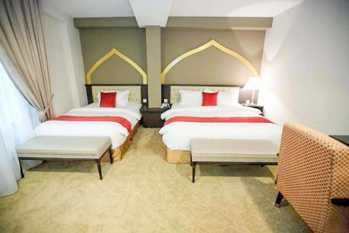 Une chambre d’hôtel avec deux lits, chacun recouvert d’une couverture rouge et blanche, et un banc au pied de chaque lit.