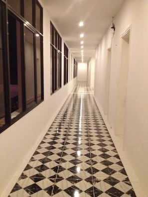 A long hallway with a black and white checkered floor, white walls, and a series of windows on one side.