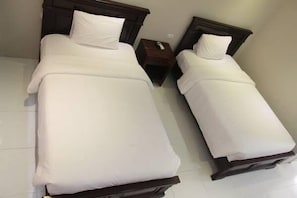 Two single beds with wooden headboards, white bedding, and a small wooden nightstand with a remote control.