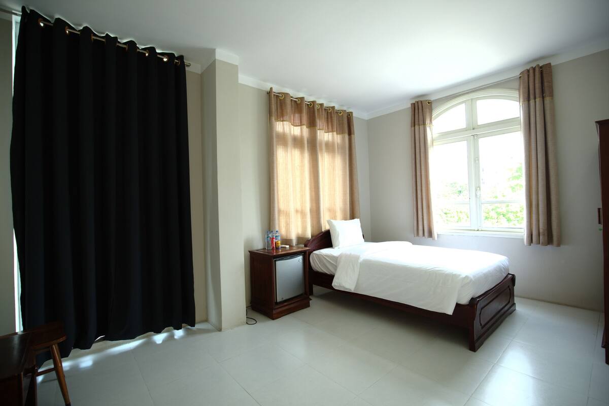 Une chambre à coucher avec un lit, une table de chevet, un bureau et une fenêtre avec des rideaux.