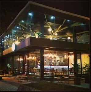 A modern building with a glass facade, outdoor seating area, and visible interior lighting. - Trang An Hotel (Hoa Lu)