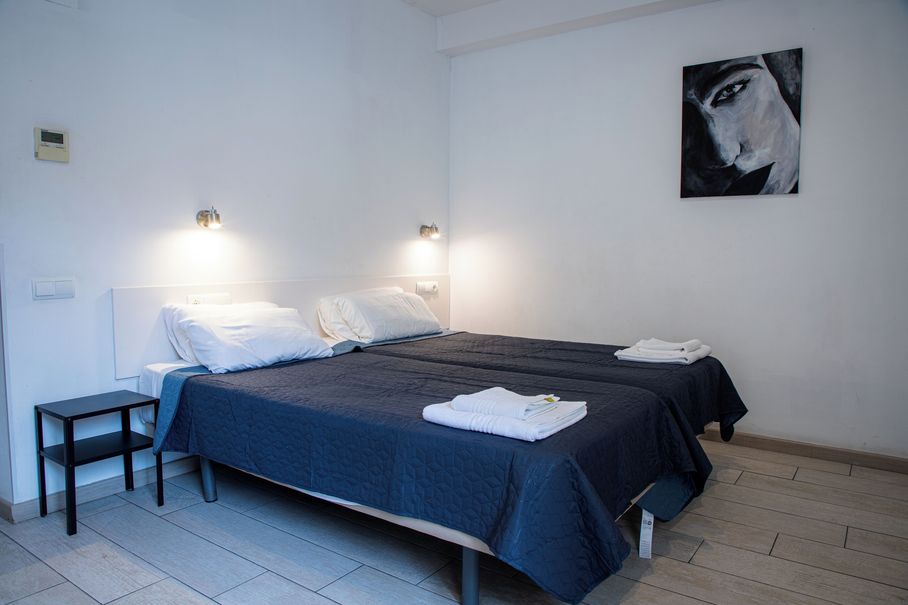 Een moderne slaapkamer met twee bedden, een nachtkastje en een schilderij aan de muur.