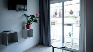 Ein modernes Wohnzimmer mit einem Flachbildfernseher, einem Blumentopf und einer Glastür, die auf einen Balkon führt.