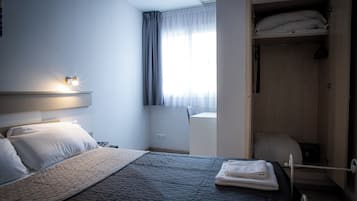 Una habitación de hotel con una cama, un armario, un escritorio y una ventana con cortinas.