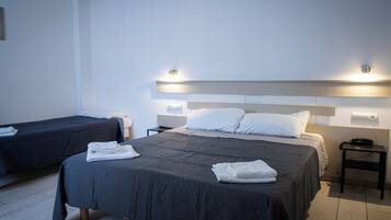 Ein Hotelzimmer mit zwei Betten, jeweils mit einer dunkel gesteppten Tagesdecke und weißen Kissen. An beiden Betten befinden sich Nachttische mit Lampen und ein an der Wand montiertes Telefon.