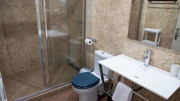 Een badkamer met een douche met glazen wand, een witte wastafel en een toilet met een blauwe zitting.