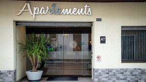 Ein Gebäudeeingang mit einem großen Topfpflanzen, einer Glastür und einem Schild mit der Aufschrift 'Apartments'.