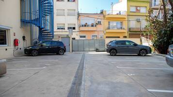 Un parking où sont garées deux voitures devant un immeuble doté d’un escalier en colimaçon bleu et de balcons.