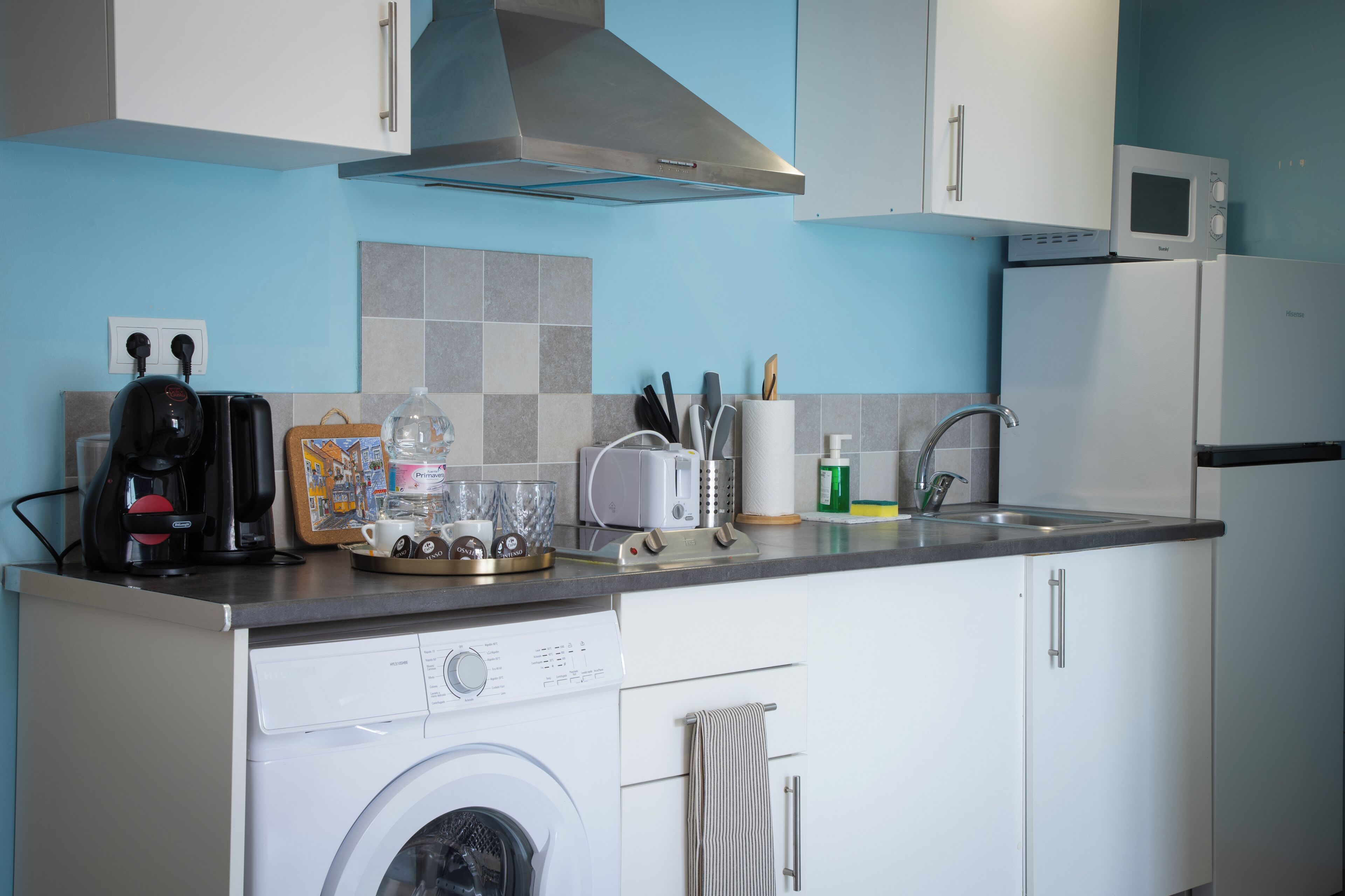 Een kleine keuken met een wasmachine, een magnetron, een broodrooster en een koffiezetapparaat.