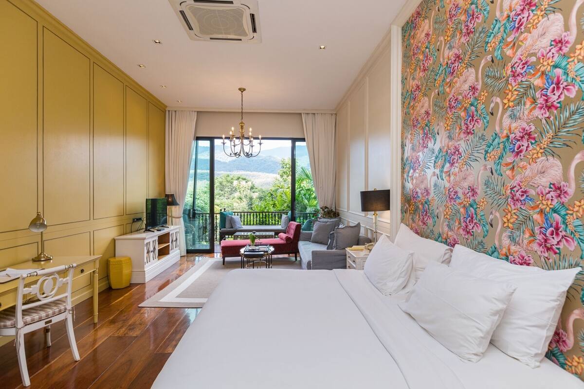 A bedroom with a large bed, a desk, a chair, a sofa, and a TV.