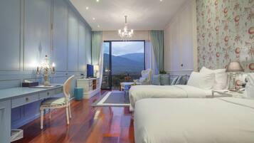 Habitación de hotel con una cama grande, un escritorio con silla, televisión y un balcón con vistas a las montañas.