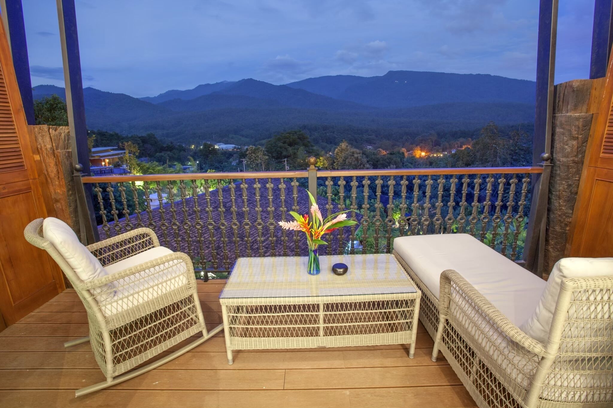 A balcony with wicker furniture, a table, and a vase of flowers.