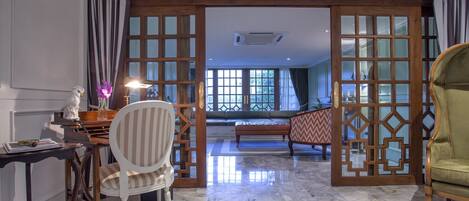 A room with a marble floor, a desk with a lamp, a chair, and a sofa. There are wooden doors with glass panels leading to another room.