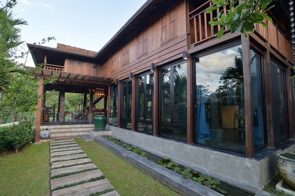 A modern house with large windows, a wooden deck, and a garden with a stone pathway.