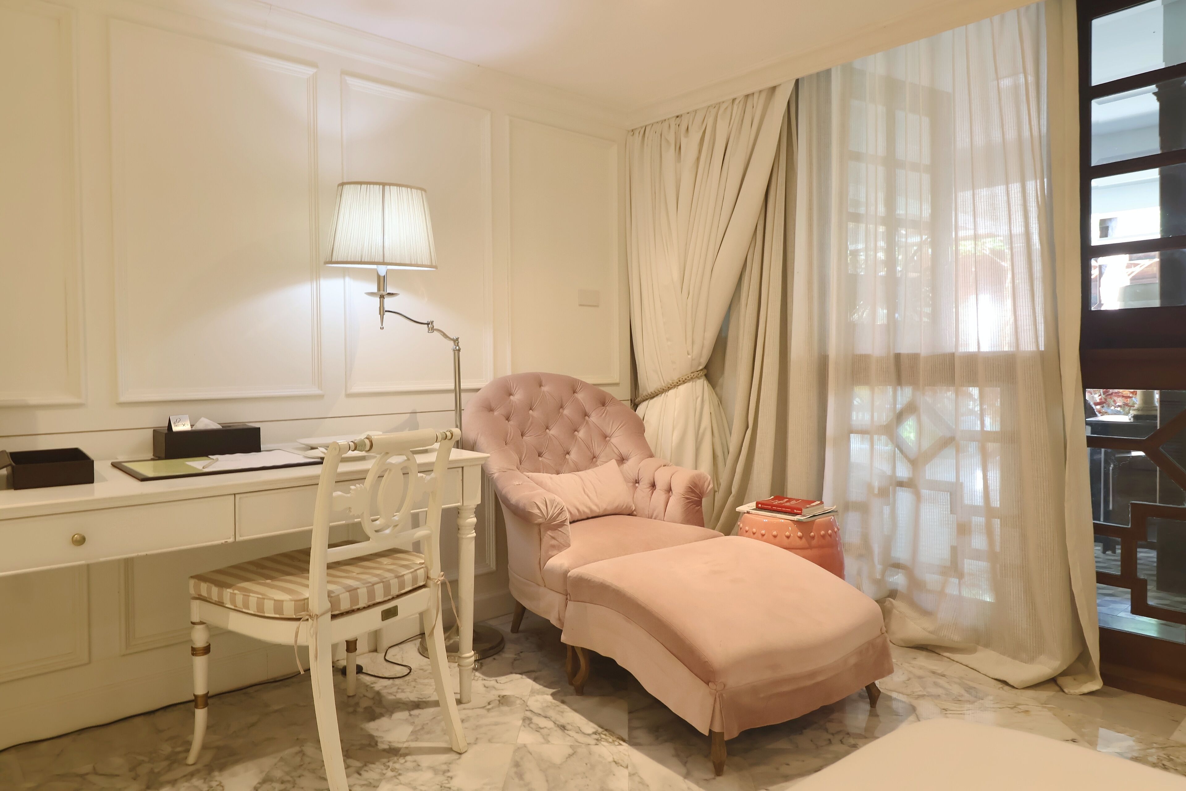 Une chambre avec un bureau blanc, une chaise rose, un lit et une fenêtre avec des rideaux.