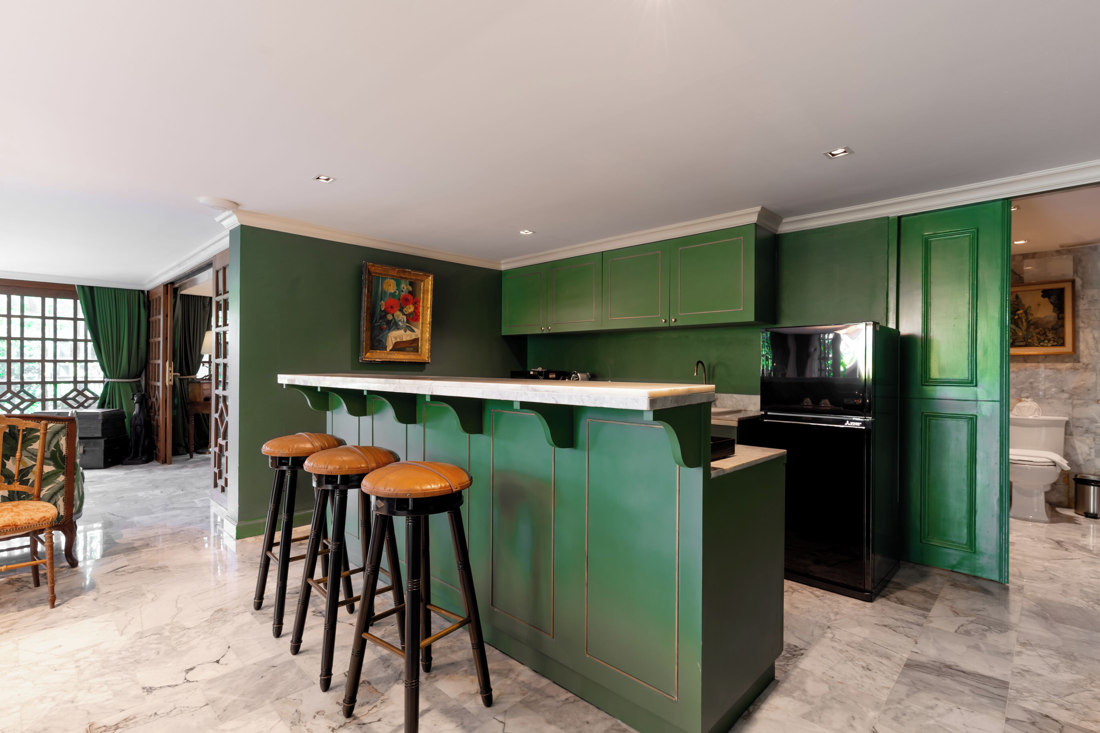 Een keuken met groene kastjes, een marmeren aanrechtblad en een zwarte koelkast.