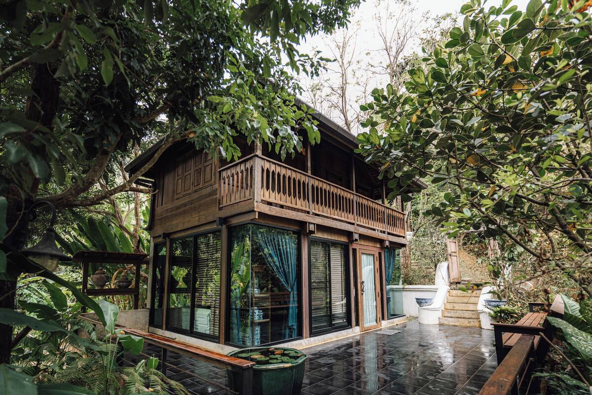 A wooden house with a balcony, surrounded by lush greenery.