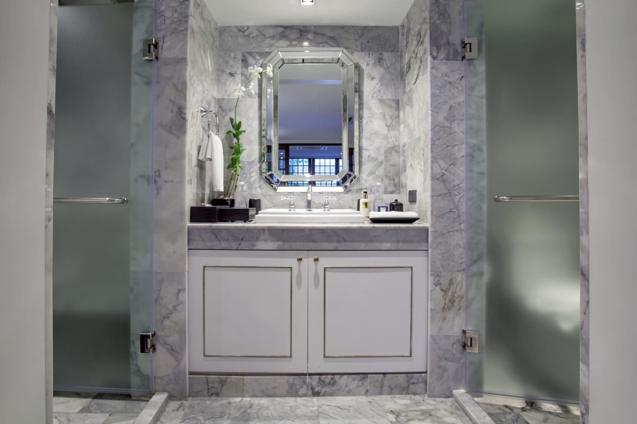 A modern bathroom with a marble vanity, a large mirror, and a glass shower enclosure.