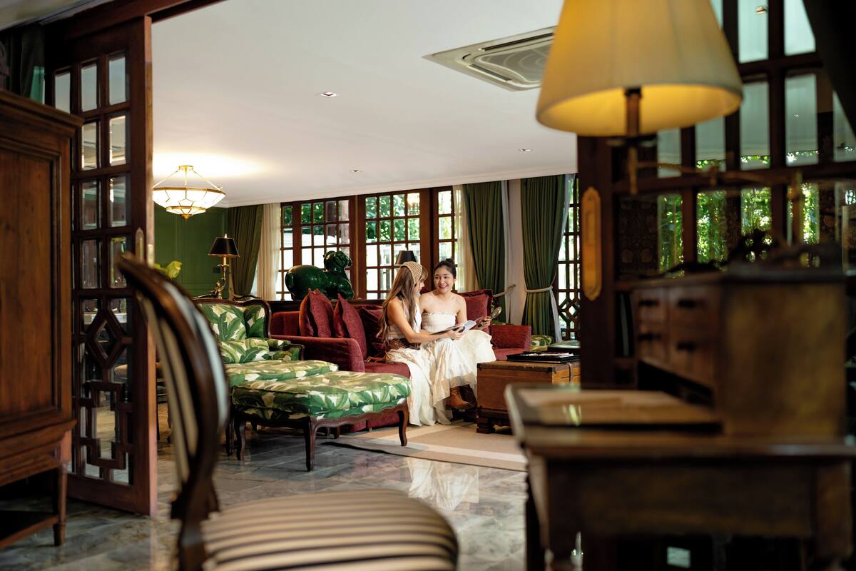 A room with a green patterned sofa, a wooden cabinet, and a large window with curtains.