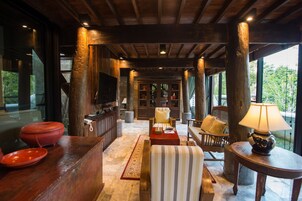 Amplio espacio interior con techo de madera, ventanas grandes y una zona de estar acogedora que incluye un sofá, sillas y una mesa.