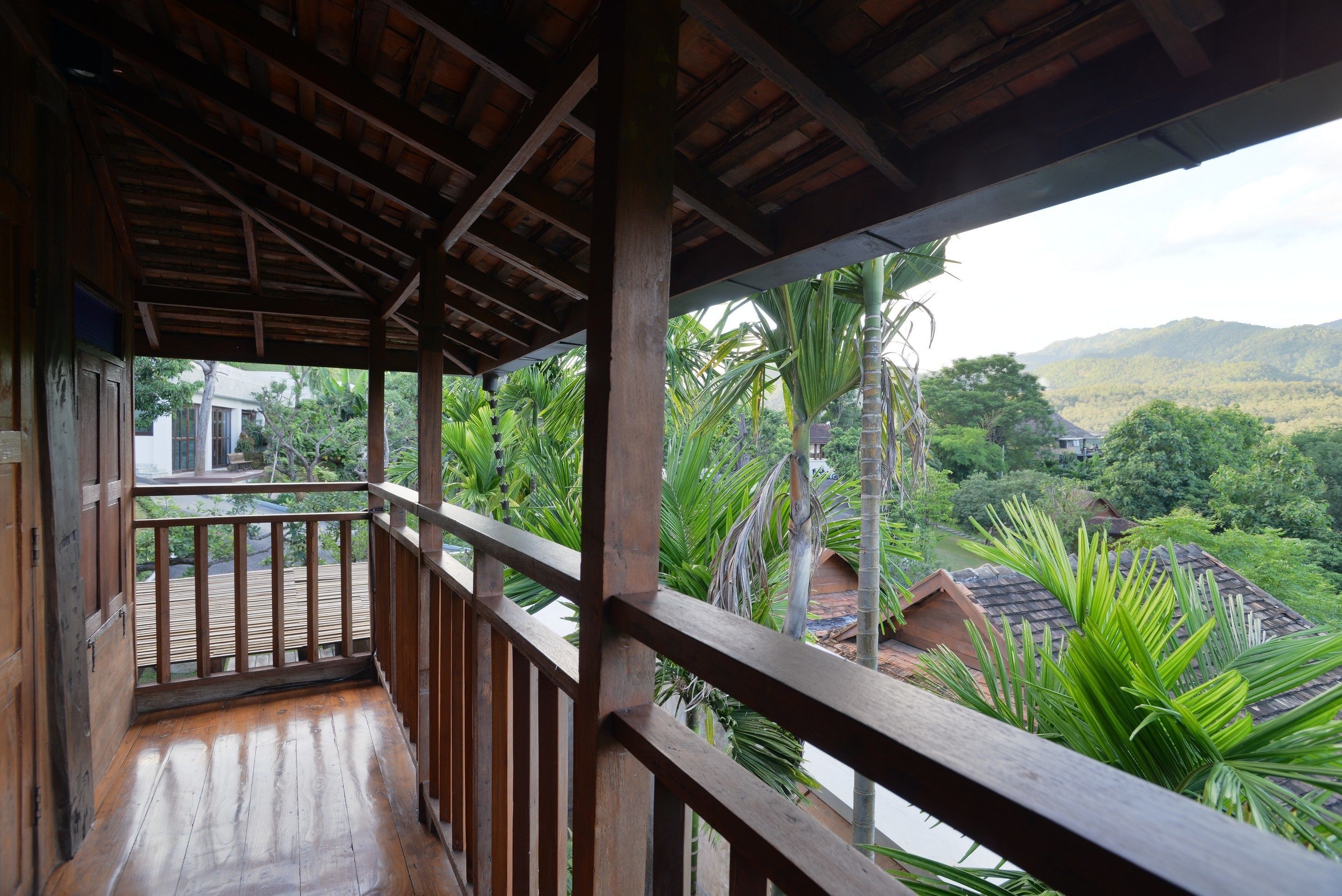 A wooden balcony with a view of a lush landscape and distant buildings.