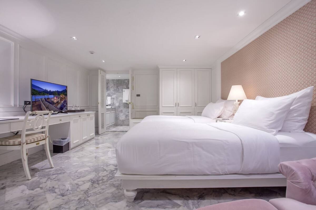 A modern hotel room with a large bed, a desk with a TV, and a bathroom visible through an open door.