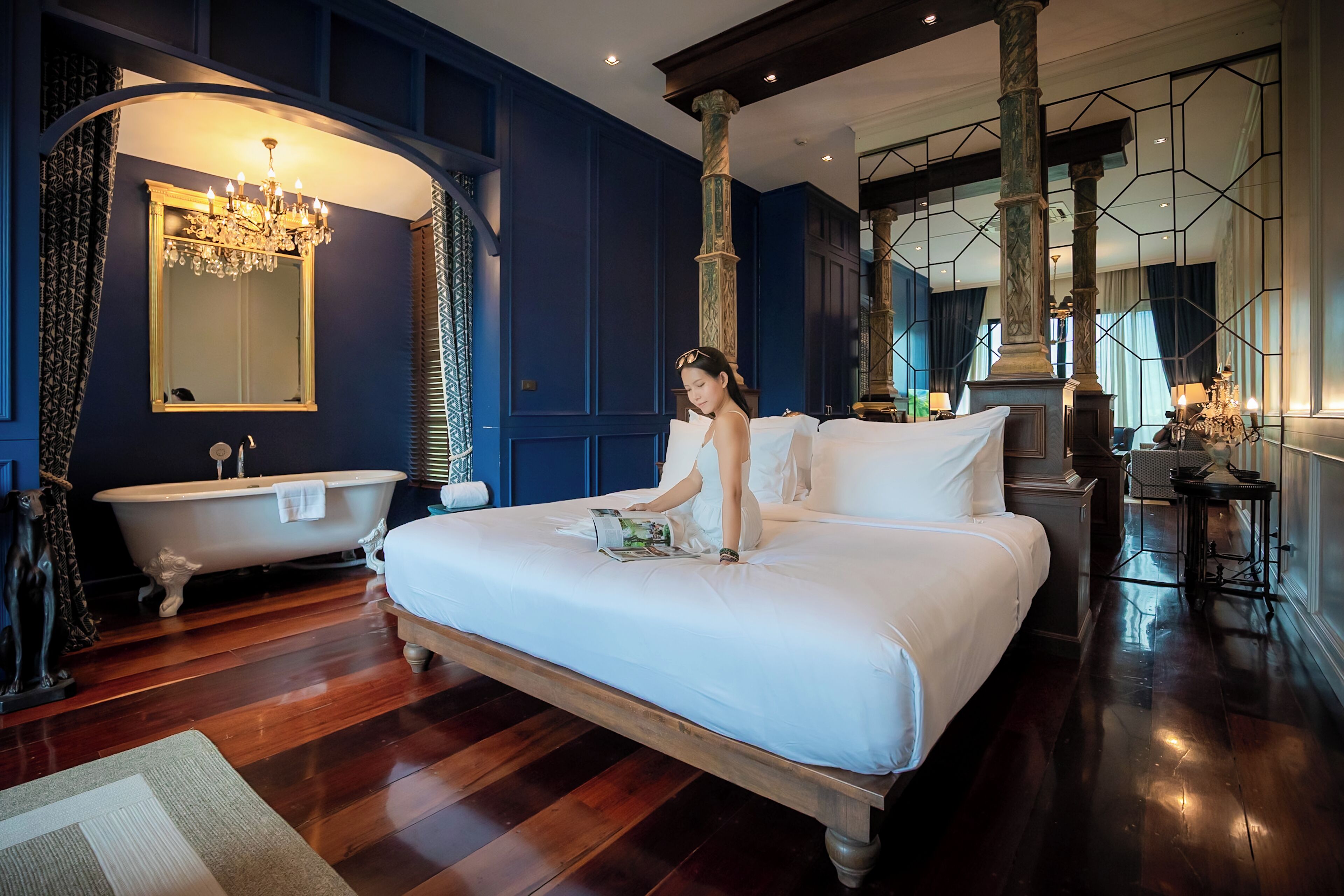A large bed with a white comforter, a vintage-style bathtub, and a chandelier.