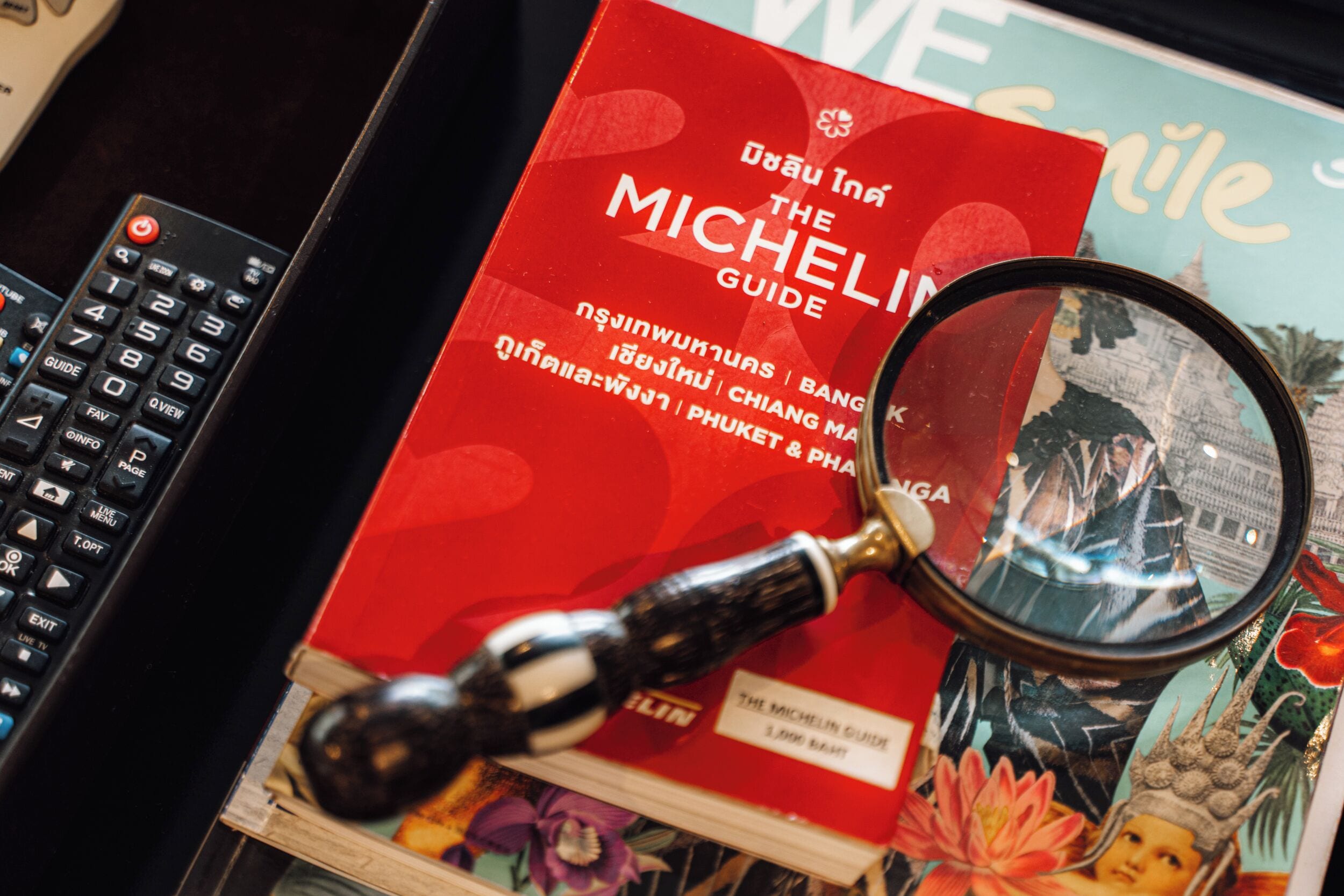 A red book titled 'The Michelin Guide' with a magnifying glass on top, placed next to a black remote control.