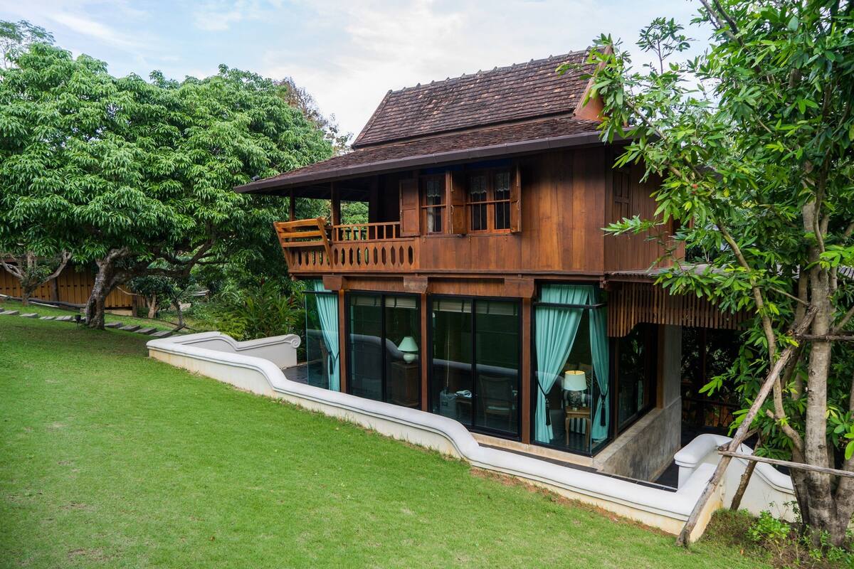 A wooden house with a balcony, large windows, and a well-maintained lawn.