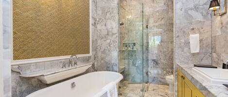 A bathroom with a freestanding bathtub, a glass-enclosed shower, marble walls, and a yellow vanity.